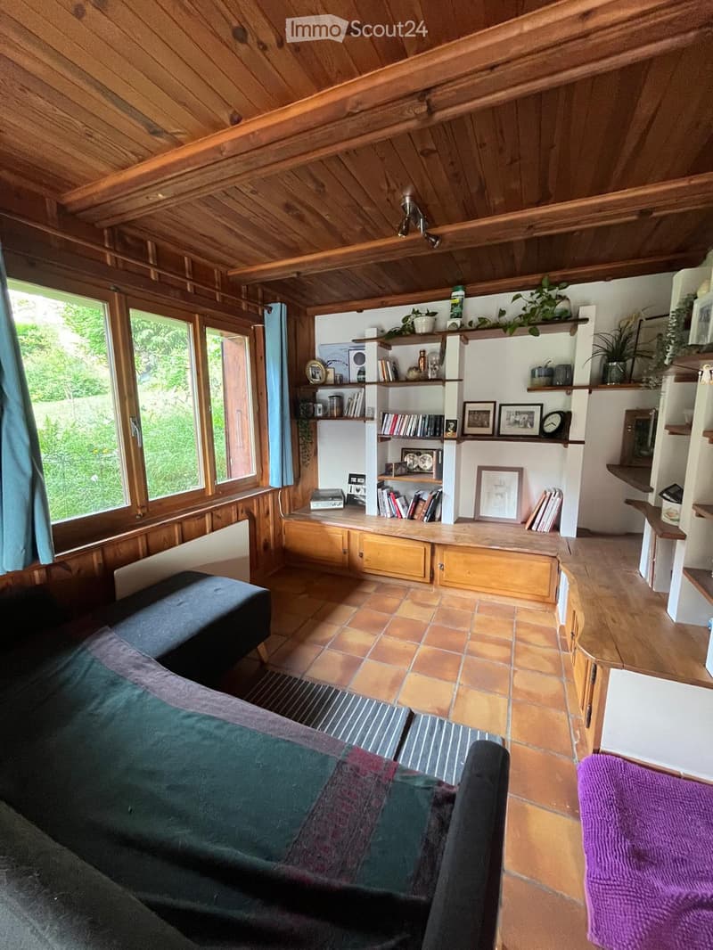Cozy living room with wooden ceiling, tiled floor, large windows, bookshelf, sofa, and decorative items.