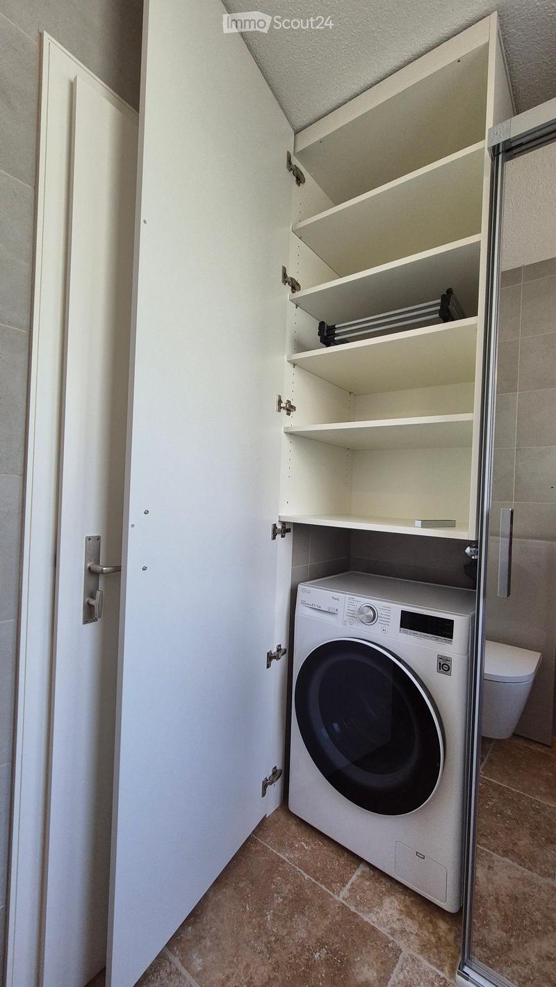 white laundry cabinet, white washer, silver shower door, white toilet, tiled flooring