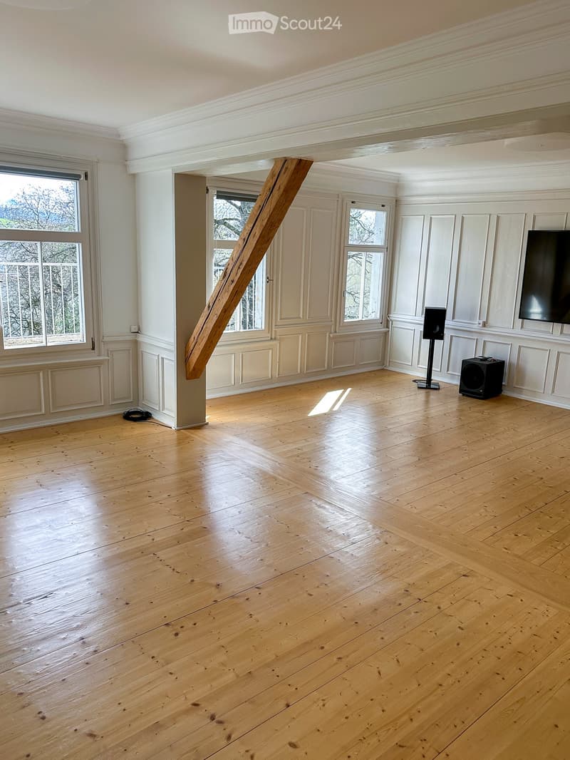 Empty room with wooden flooring, white walls, large windows, and a wooden pillar. No furniture or equipment present.