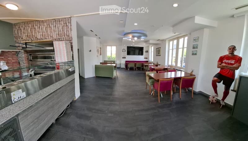 Modern restaurant interior with a kitchen counter on the left, dining tables and chairs in the center, and a sofa area near the windows.