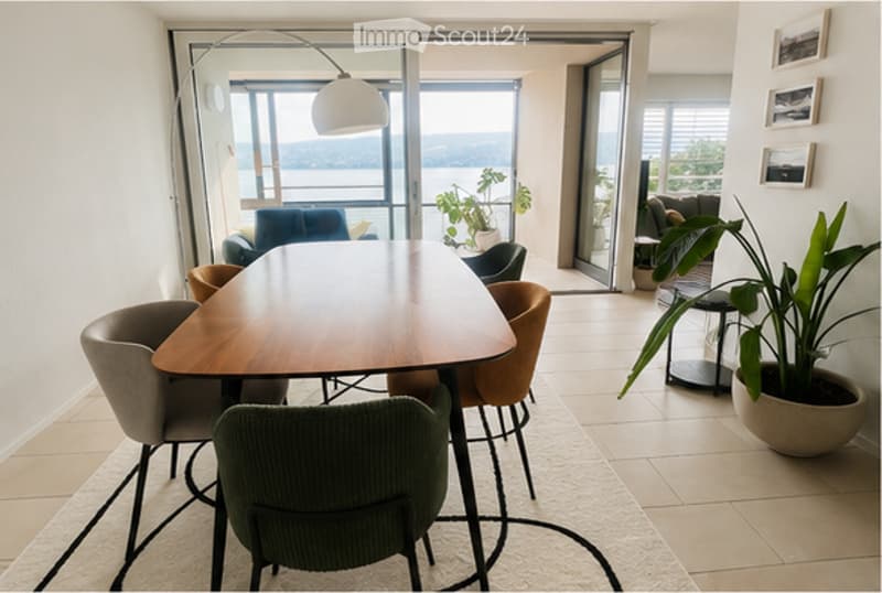 Bright dining area with a wooden table, six chairs, a sofa, and a large window offering a scenic view.
