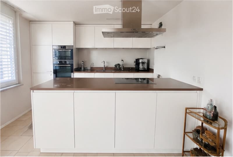 Modern kitchen with white cabinets, dark countertops, a central island, built-in oven, and a wine rack in the corner.