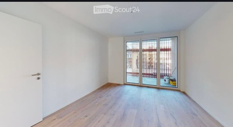 Empty room with light wooden flooring, white walls, and large sliding glass doors leading to an outdoor area.