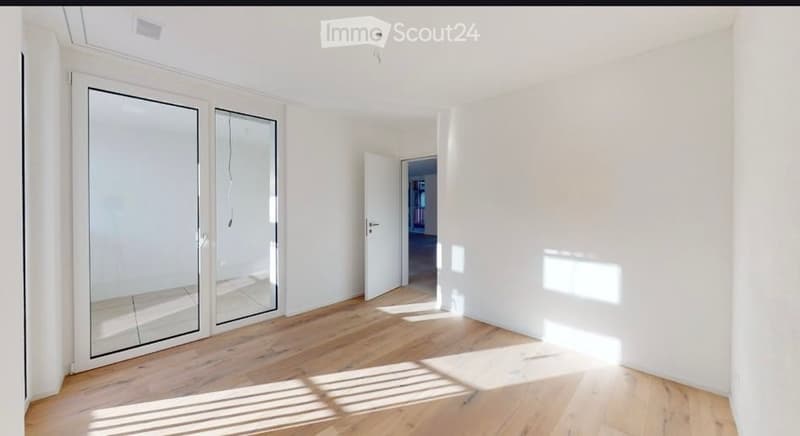 Empty room with white walls, wooden floor, large glass sliding doors, and natural light coming in.