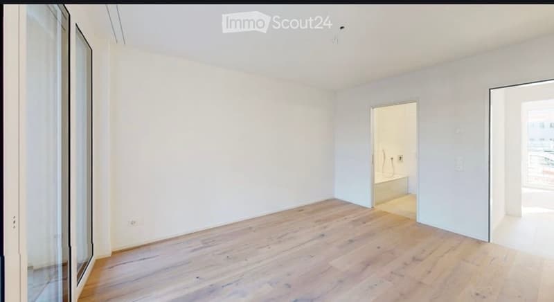 Empty room with light wooden flooring, white walls, and large windows. No furniture or equipment present.