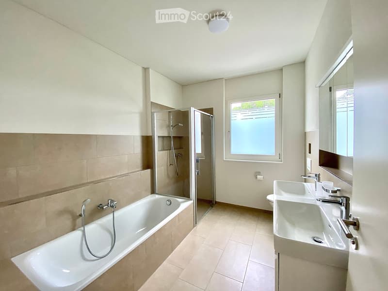 Modern bathroom with a bathtub, double sink, shower, and large window providing natural light.