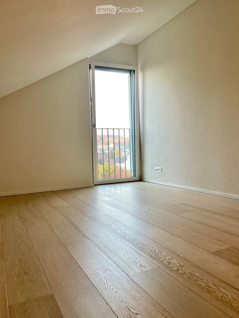Empty room with light wooden flooring, white walls, and a sliding glass door leading to a balcony.