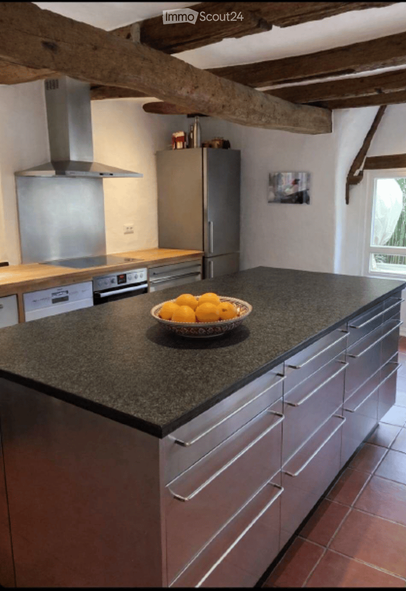 Modern kitchen with stainless steel appliances, granite island, and a bowl of oranges on the counter.