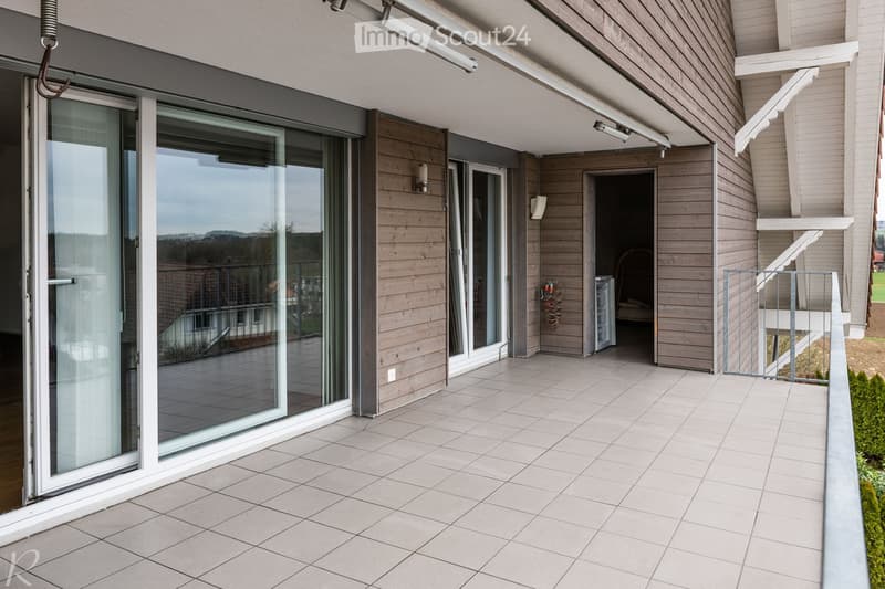 Balcony with tiled floor, large sliding glass doors, wooden walls, and a view of the landscape.
