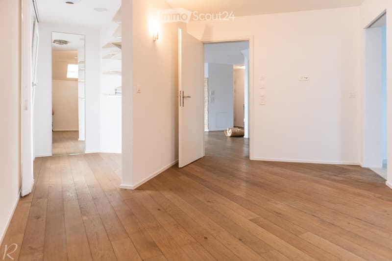 Empty hallway with wooden flooring, white walls, and open doors leading to other rooms.