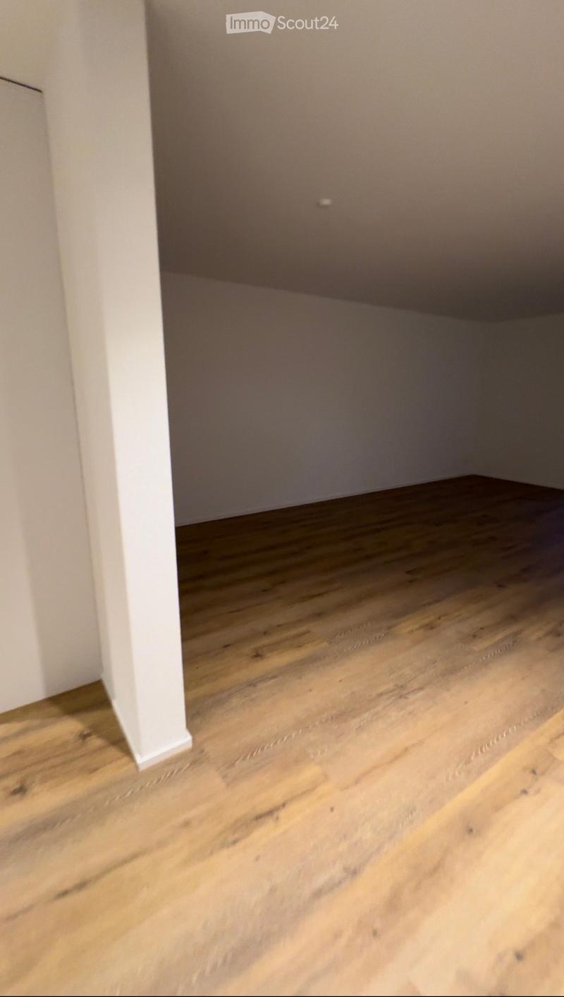 Empty room with wooden flooring and white walls, featuring a visible doorway leading to another space.