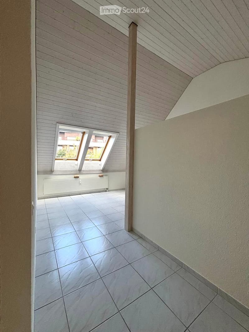 Empty room with wooden slatted ceiling, tiled floor, and a skylight window offering a view of the outside.
