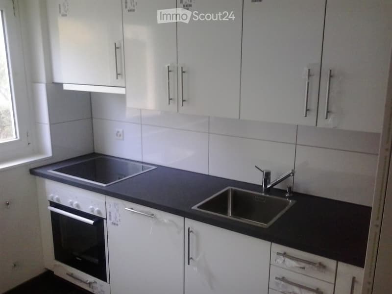 Modern kitchen with white cabinets, black countertops, an oven, a sink, and a faucet.