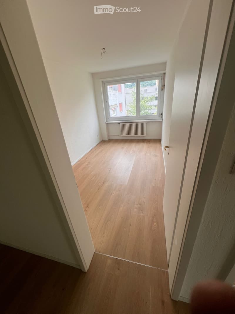 Empty room with wooden flooring, white walls, and a window with a radiator below it.