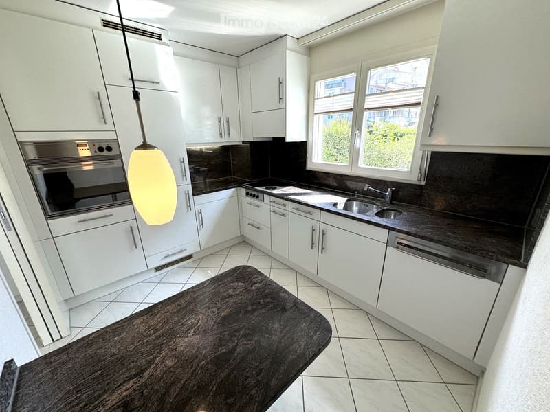 Modern kitchen with white cabinets, stainless steel appliances, dark countertops, and a central island.