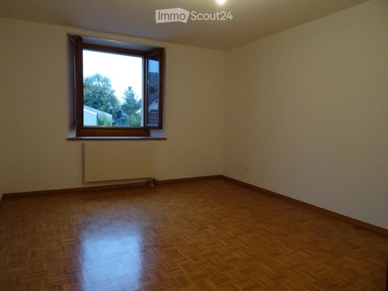 Empty room with wooden flooring, white walls, and a single window with a radiator below it.