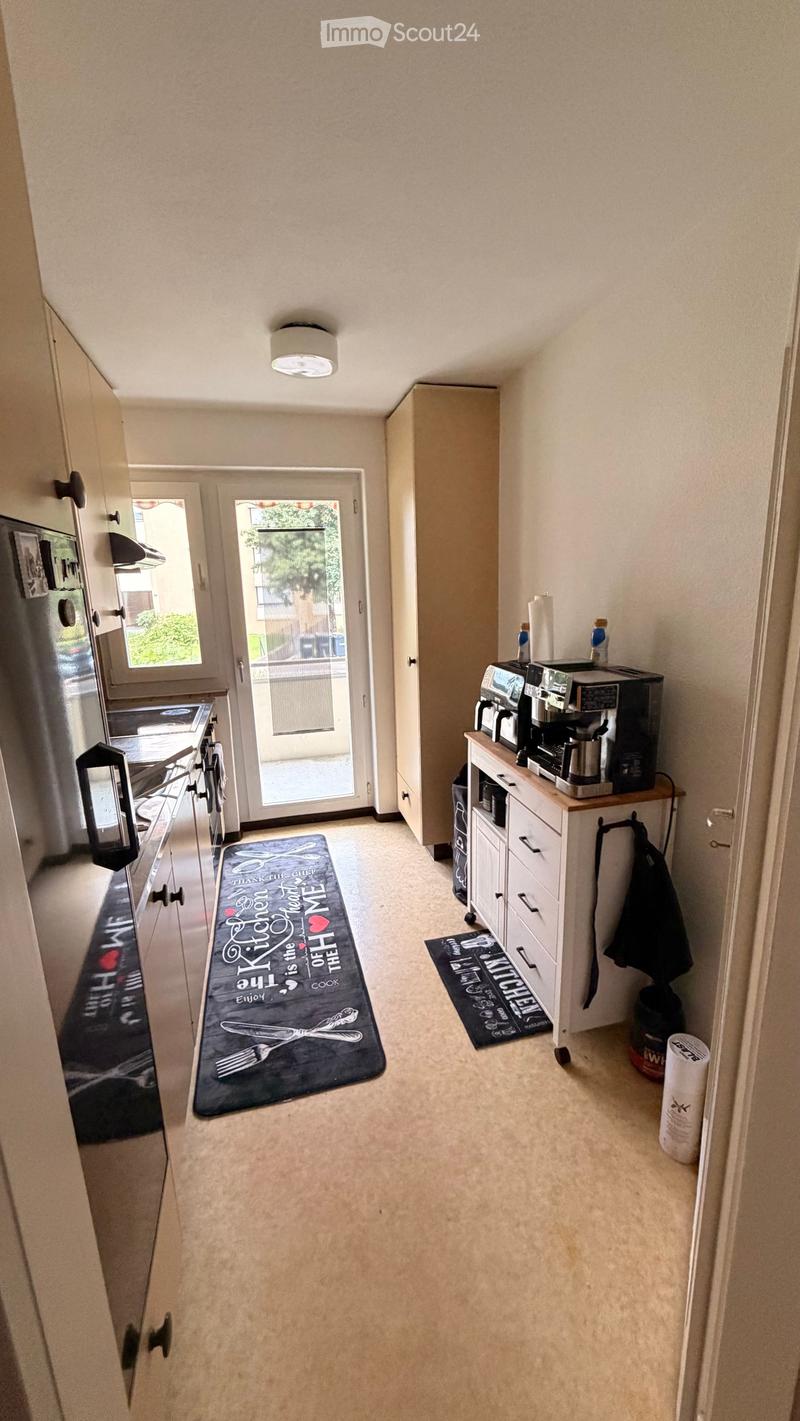 A modern kitchen with white cabinets, a refrigerator, an oven, a coffee maker on a small counter, and two decorative rugs on the floor.
