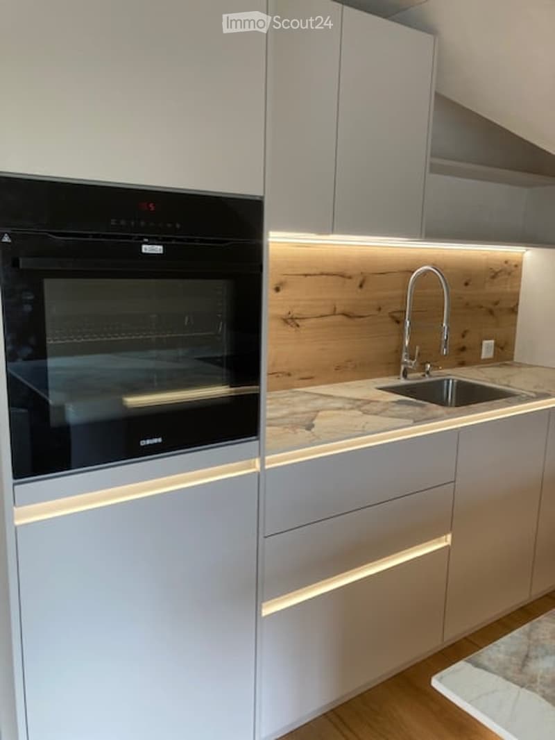 Modern kitchen with sleek grey cabinets, a built-in oven, a wooden backsplash, and a stainless steel sink with a modern faucet.