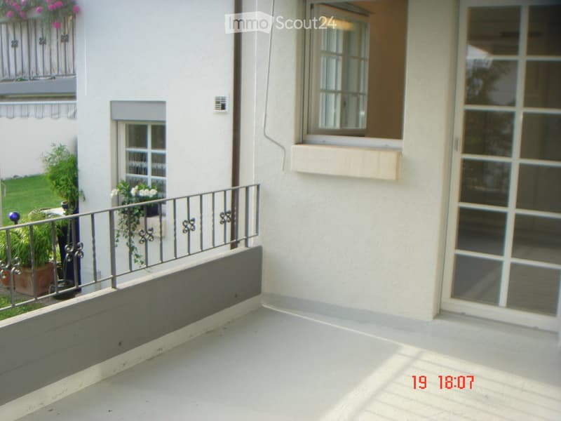 Balcony with white tiled floor, metal railing, and potted plants visible on the adjacent terrace.