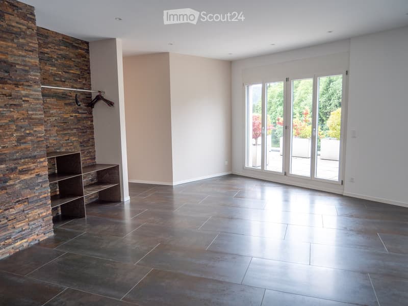 Empty room with dark tiled floor, stone fireplace, built-in bench, and large glass doors leading to outdoor area.