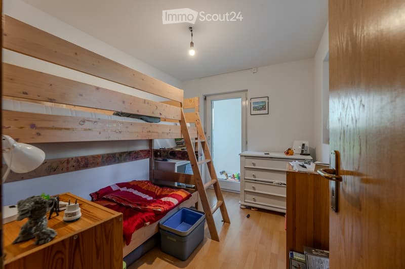 Cozy bedroom with a wooden bunk bed, a small table with a lamp, a dresser, and a picture frame on the wall.