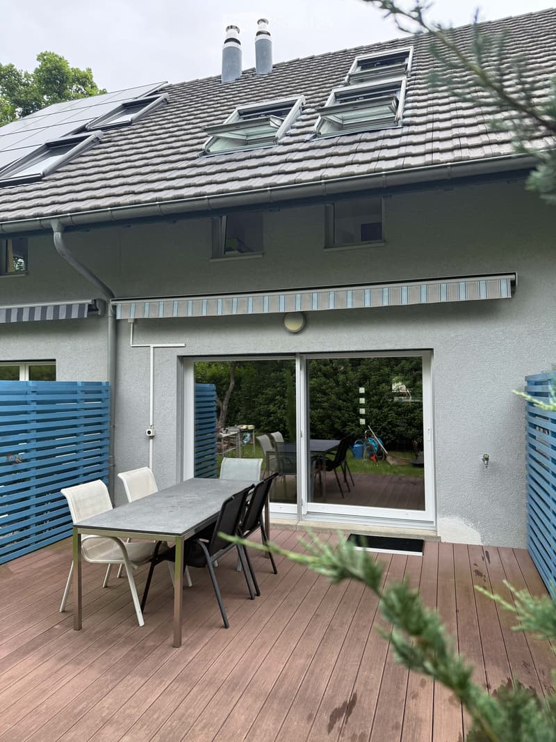 Wooden deck with a table and chairs, large sliding glass doors leading to the house, blue lattice fencing, and a view of the garden.