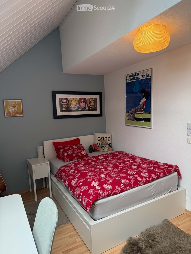 Cozy bedroom with a white bed, red bedding, nightstand, chair, and framed pictures on the walls.