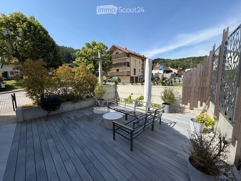 Wooden deck with a bench, chairs, tables, and potted plants, overlooking a residential area with houses and trees.