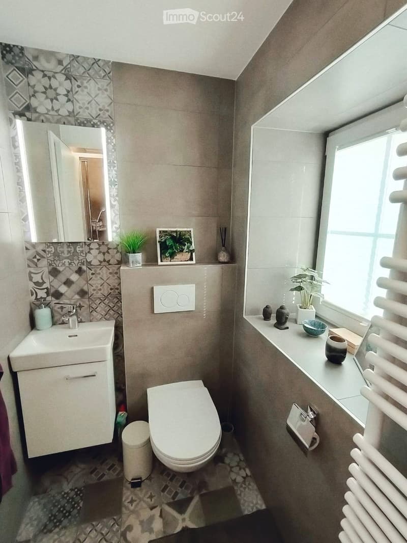 Modern bathroom with a sink, mirror, toilet, and decorative items including a picture frame, vase, and plant on the windowsill.