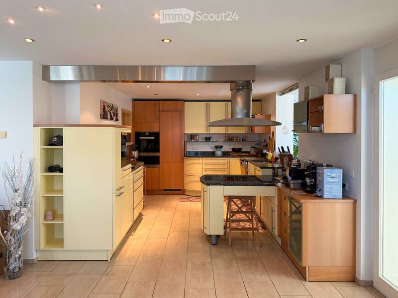 Modern kitchen with light wooden cabinets, stainless steel appliances, and a central island with bar stools.