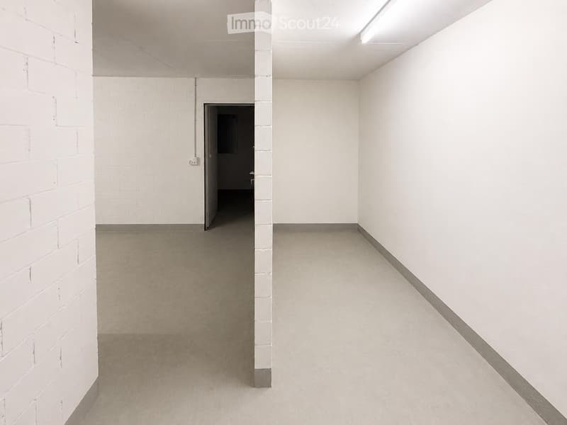Empty hallway with white brick walls, concrete floor, and a single doorway leading to another room.