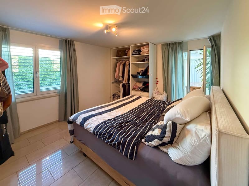 A well-lit bedroom with a large bed, a wardrobe, and large windows with curtains.