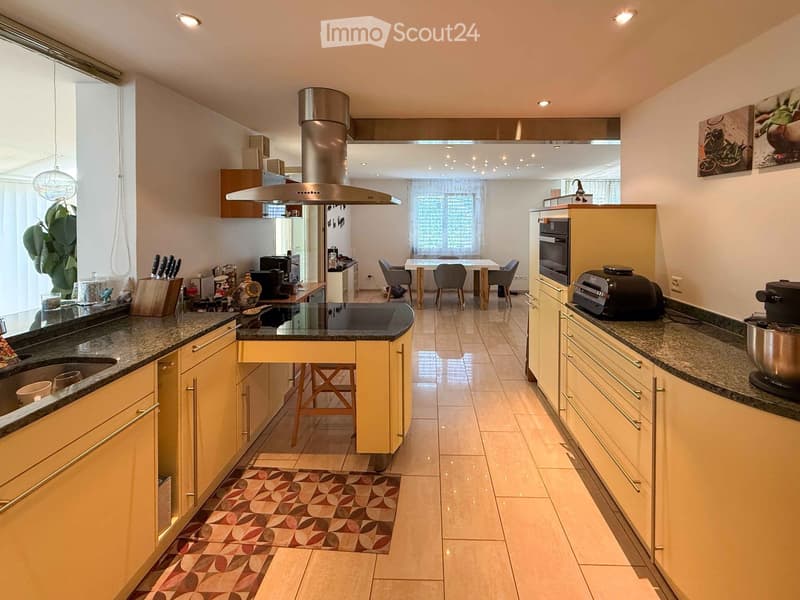Modern kitchen with light-colored cabinets, granite countertops, and a central island. Features include a sink, stove, oven, microwave, and a small dining area with a table and chairs.