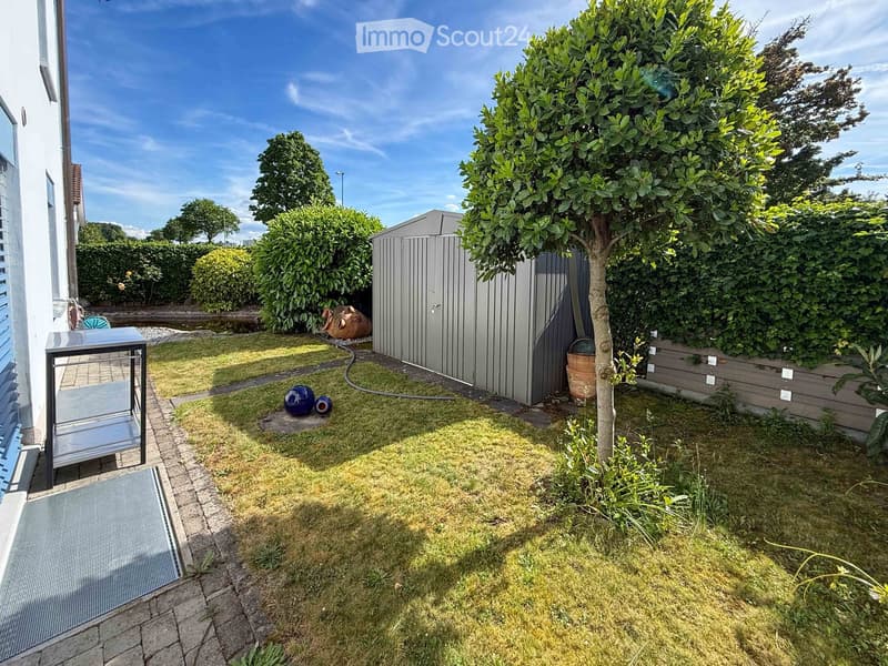 Well-maintained garden with a lawn, a tree, a shed, and decorative items including a blue sphere and a small table with chairs near the house.