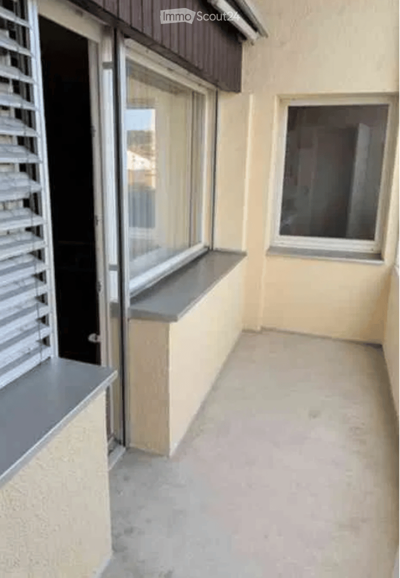 Balcony with beige walls, grey window sills, and a view of the street through the windows.
