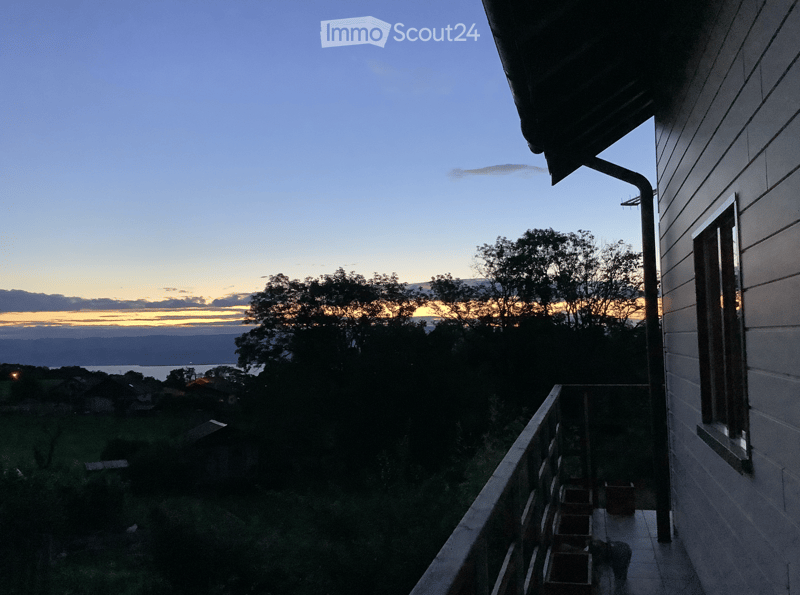 Balcony overlooking a scenic view of a lake and distant hills during sunset, with a few potted plants on the balcony.