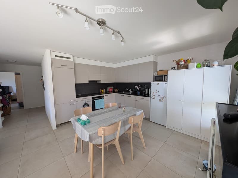 Modern kitchen with light grey cabinets, a dining table with four chairs, and various appliances including a refrigerator, microwave, and oven.