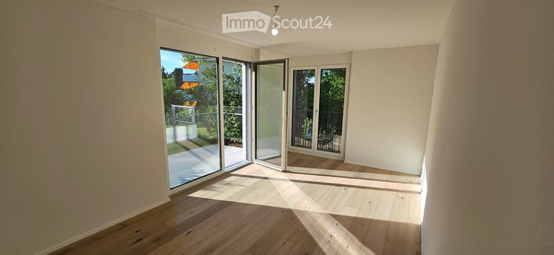 Empty room with wooden flooring, large sliding glass doors leading to an outdoor area, and natural light streaming in.