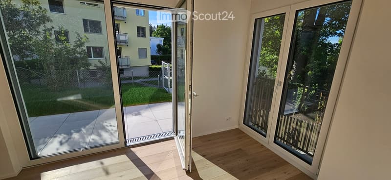 Empty room with wooden flooring and large glass sliding doors leading to a balcony and outdoor area.