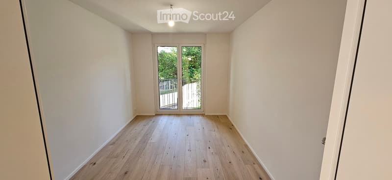 Empty room with light wooden flooring, white walls, and a large glass door leading to a balcony or outdoor area.