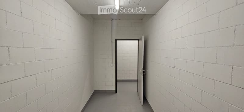 Empty hallway with white brick walls, a single open door leading to another room, and a visible electrical outlet on the wall.