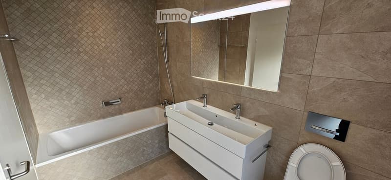 Modern bathroom with a large bathtub, double sink, toilet, and a large mirror with LED lighting.