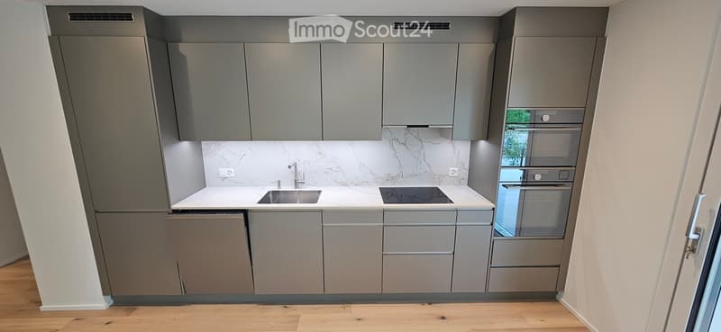 Modern kitchen with grey cabinets, white marble backsplash, stainless steel sink, stove, and built-in oven.