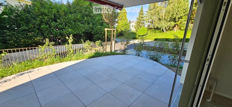 Balcony with tiled floor, metal railing, and view of a green garden and trees.