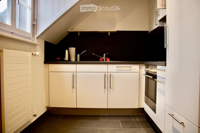 Modern kitchen with white cabinets, stainless steel oven, dark countertops, and a window above the sink.