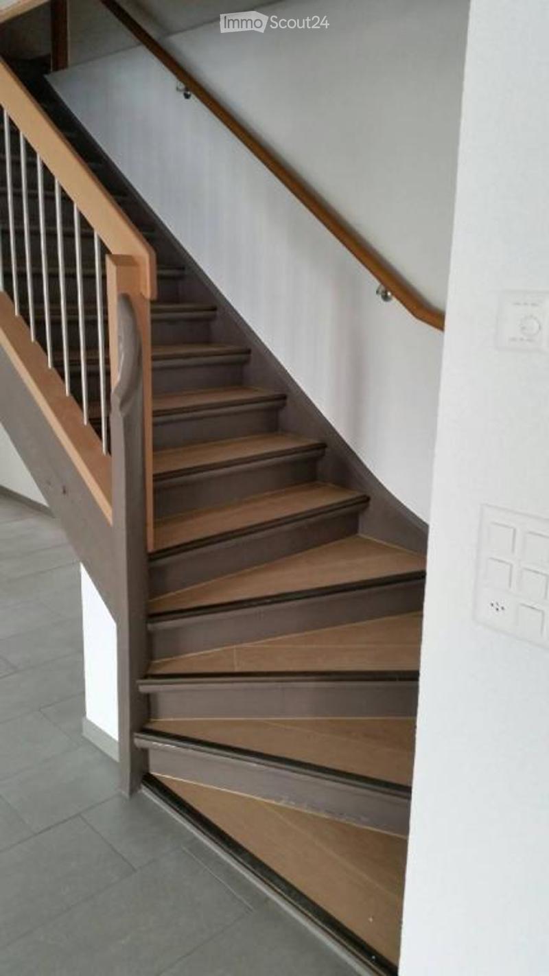 A modern staircase with wooden steps and a metal railing, leading upwards in a well-lit interior space.