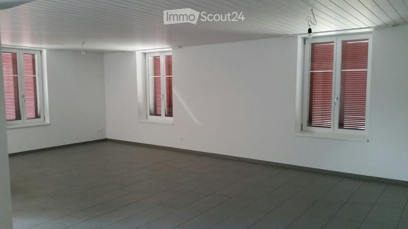 Empty room with white walls, tiled floor, and three windows with red blinds. No furniture or equipment present.
