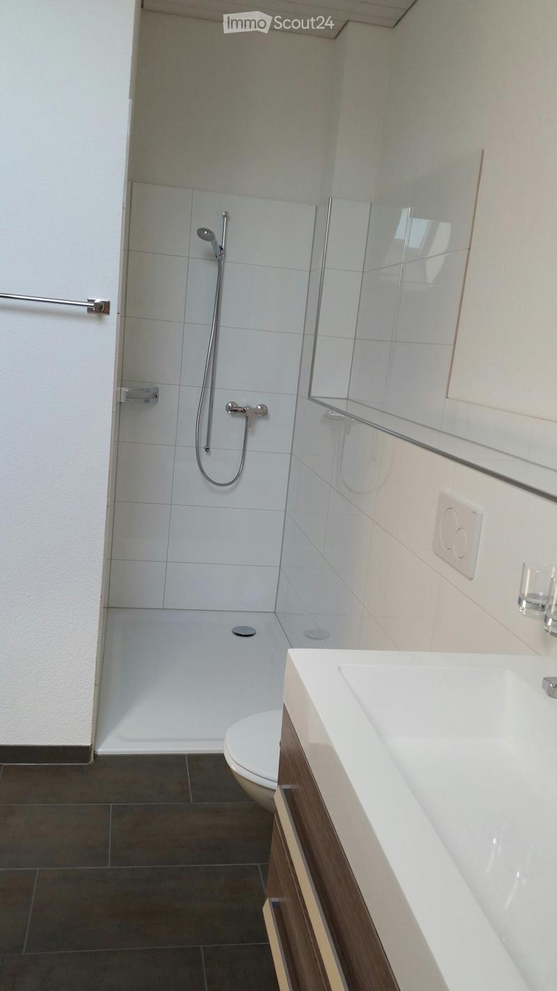 Modern bathroom with white tiles, a glass-enclosed shower, a white sink with wooden cabinet, and a toilet.