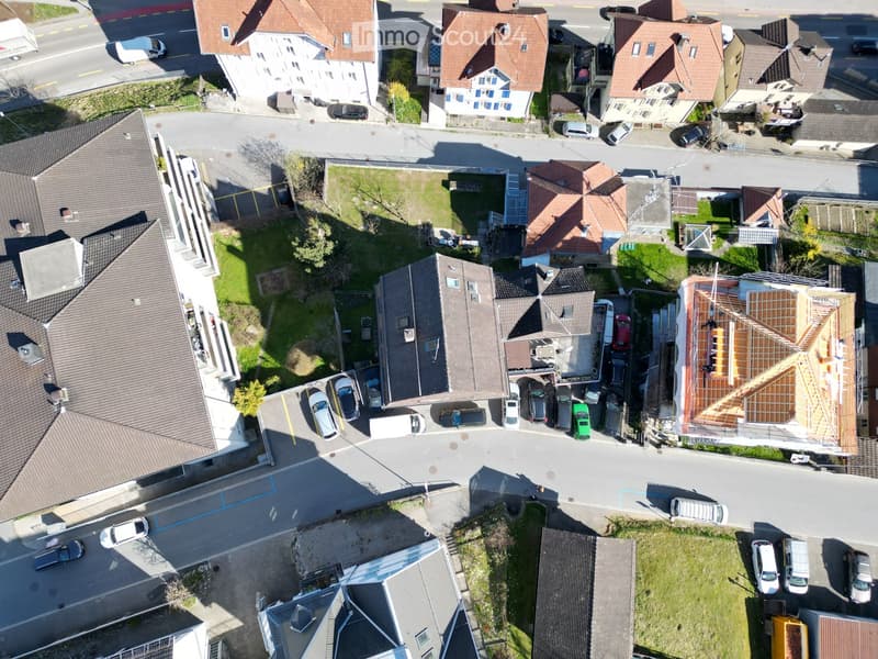 Aerial view of a residential neighborhood with multiple houses, parked cars, and a construction site with exposed wooden framing on one roof.
