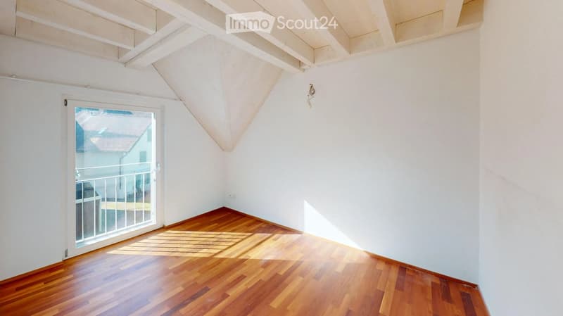 Empty room with wooden flooring, white walls, and a large window with a view of a balcony and outdoor area.